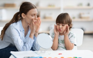 Cute little boy with speech problems practicing with therapist, doing practice and looking at mirror, free space