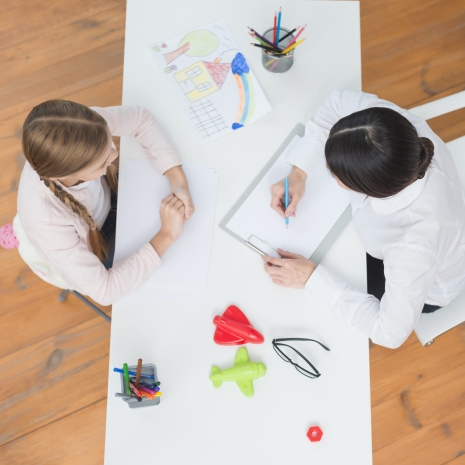 elevated-view-little-girl-talking-with-her-female-psychologist-taking-note-clipboard